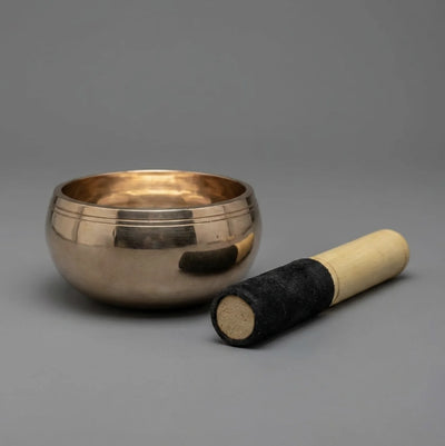 Polished bronze Kansa singing bowl with wooden mallet, 45-degree angle, grey background — handcrafted by Copper Mart